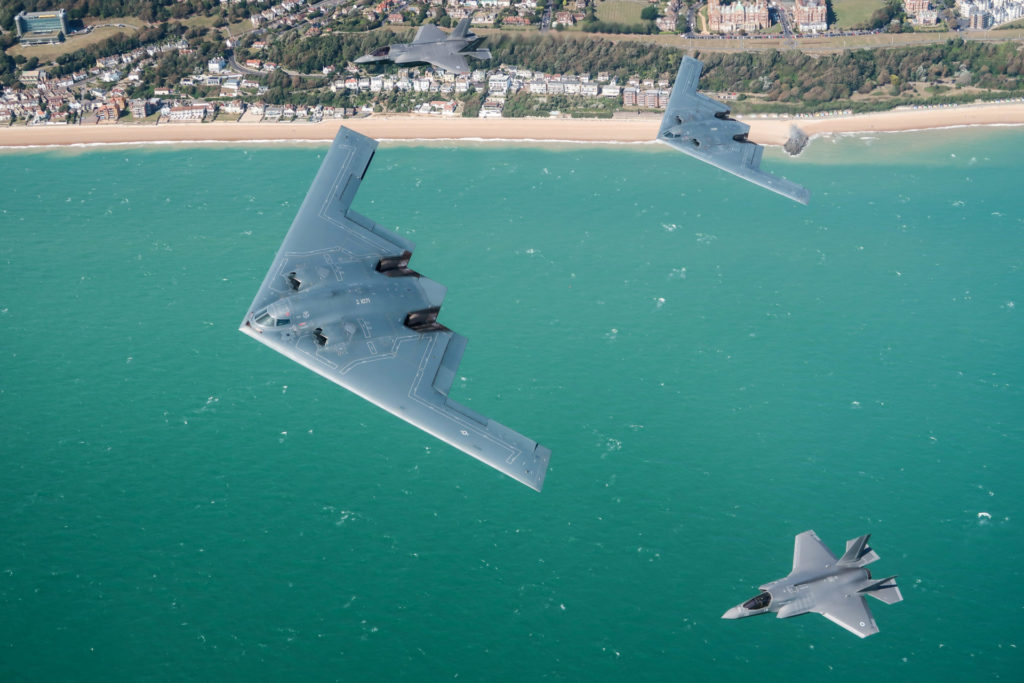 A United States Air Force B2 Spirit, currently deployed to RAF Fairford in Gloucestershire, flies above the English countryside near Dover with two RAF F-35 jets. For the first time, UK F-35 Lightning jets have been conducting integration flying training with the B-2 Spirit stealth bombers of the United States Air Force as part of their deployment to RAF Fairford in Gloucestershire, UK. The USAF deployment of the B-2’s from the Bomber Task Force Europe is long-planned. Whilst deployed to the UK the aircraft will conduct a series of training activities in Europe. During this deployment, RAF F-35B Lightning fighters are conducting sorties with the USAF B-2 bombers. Both are 5th generation aircraft and this is the first time that USAF B-2’s have trained with non-US F-35’s. RAF Fairford routinely hosts deployments and exercises by US strategic aircraft. These regular deployments reinforce the US Air Force Europe and the Royal Air Force’s unique and complementary partnership and our collective contribution to NATO. Imagery captured by a USAF Exchange Pilot.
