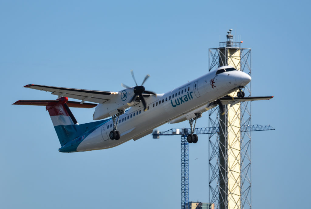 A Dash 8 climbs out from London City Airport past the new digital control tower mast